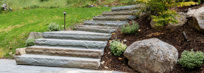 Split face bluestone steps with rock garden and outdoor lighting curving around a hill in Woodstock, NY by Masseo Landscape, Inc.