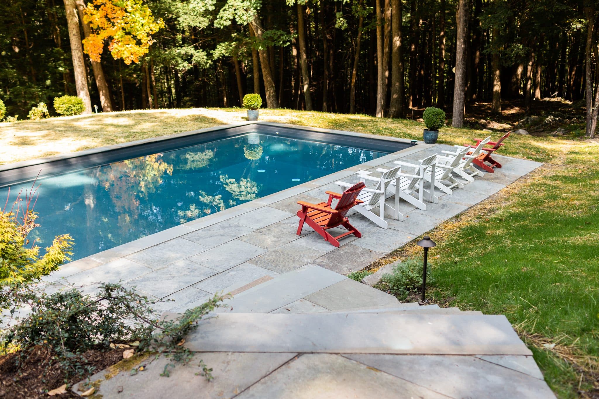 A pool with a bluestone patio and colorful chairs in the sunlight in Woodstock, NY.