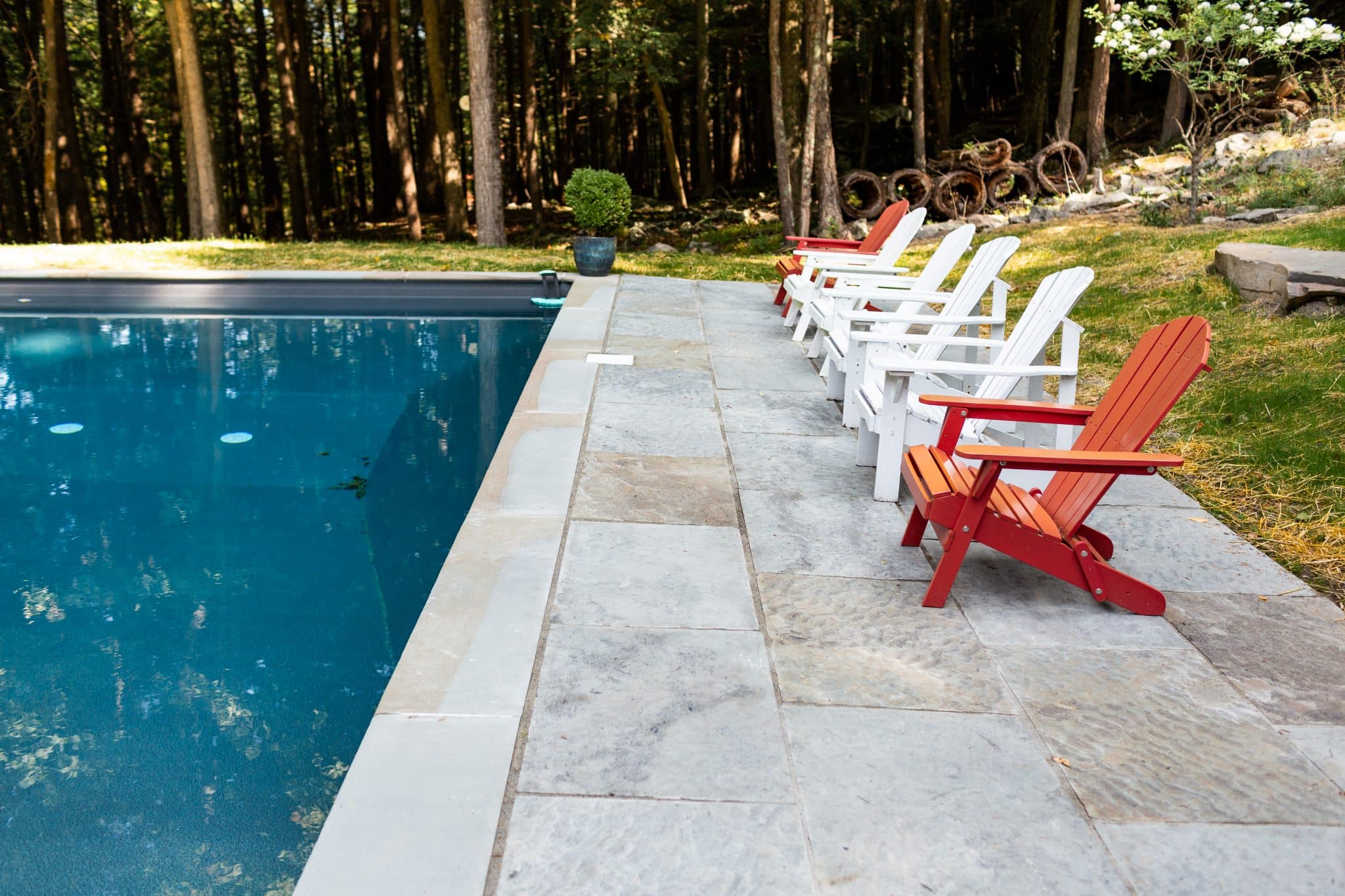 A geometric cut bluestone patio next to a pool with matching bluestone coping and colorful Adirondak chairs in Woodstock, NY.