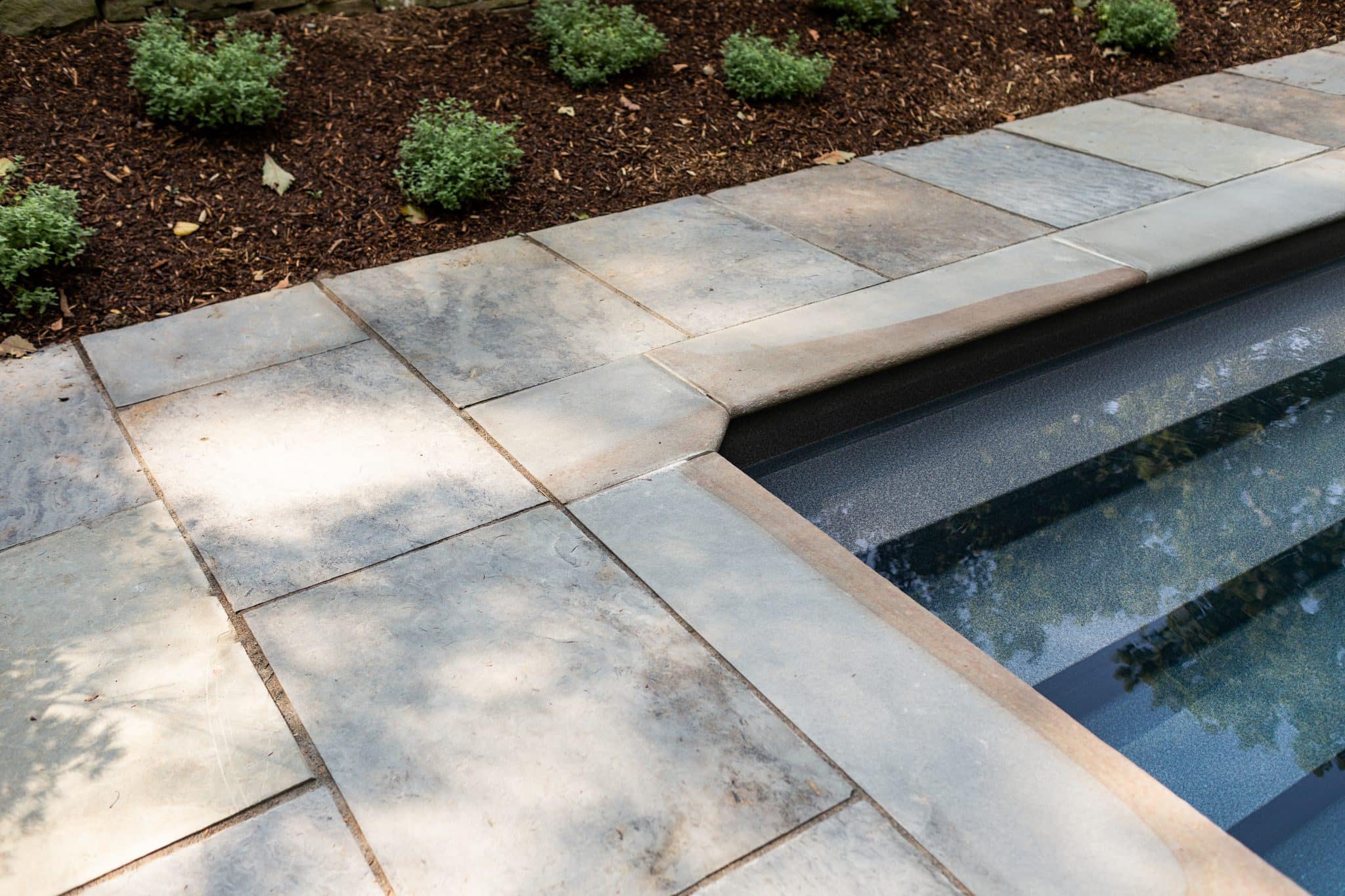 A detail highlighting geometric cut bluestone patio with natural color bluestone coping on a pool corner.