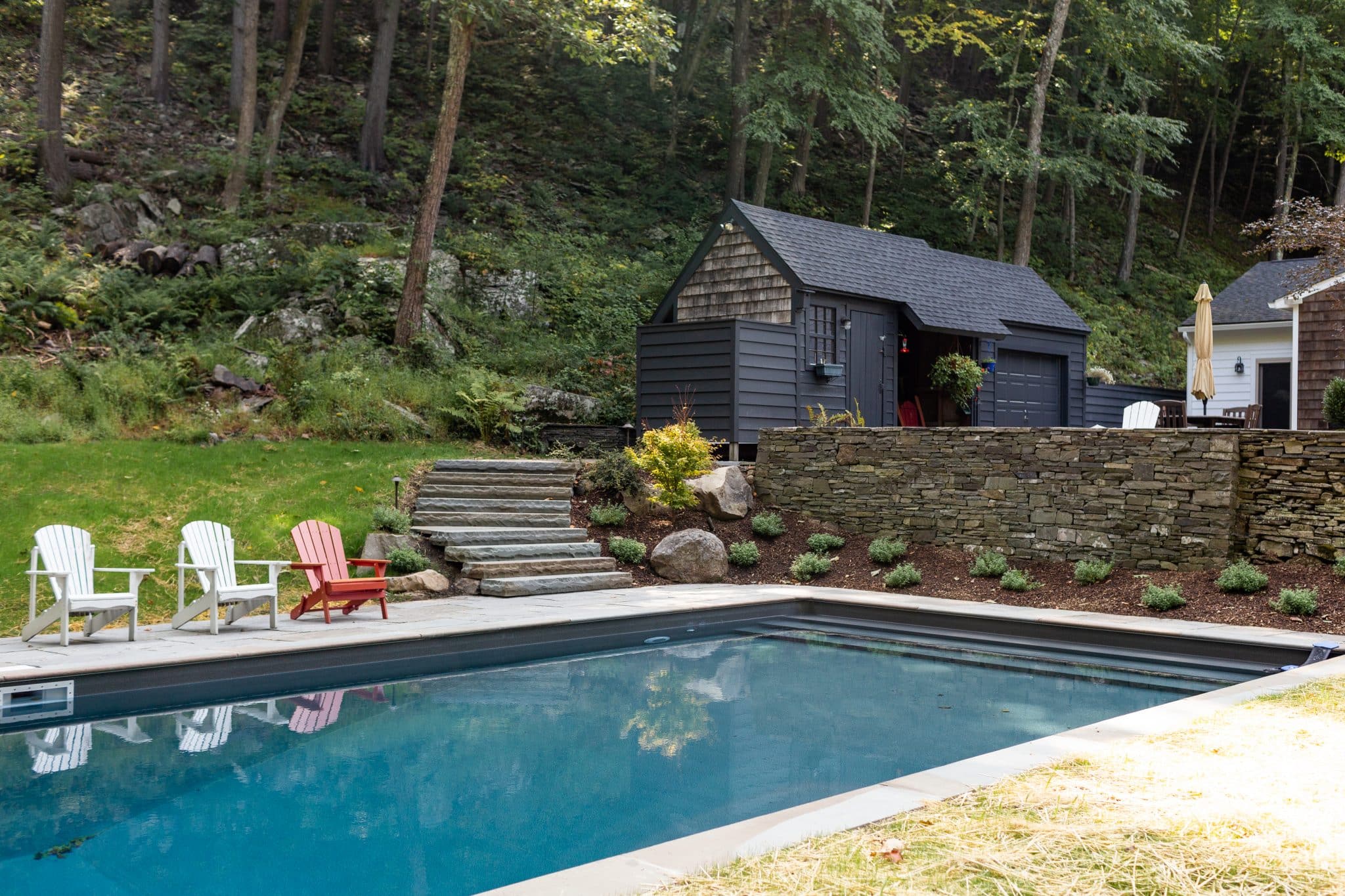 A pool with a bluestone patio and bluestone coping with split face steps to a higher patio and planting spaces planted with native plants in Woodstock, NY.