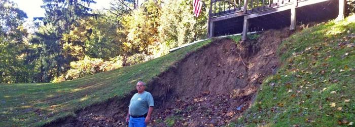 Image of man next to his home with eroded landscape endangering his home.