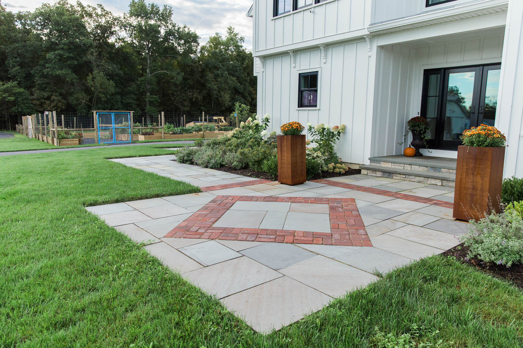 A geometric cut bluestone entryway landing with a diamond-shaped recycled brick inlay and metal planters in front of a modern farmhouse in Gardiner, NY, designed and installed by Masseo Landscape, Inc., Gardiner Landscapers
