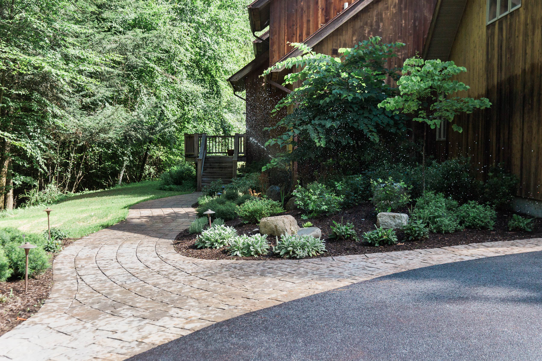 A curving paver front entry path with planting beds and outdoor lighting on either side with built-in irrigation in Cottekill, NY, designed and installed by Hudson Valley Landscaper Masseo Landscape, Inc.